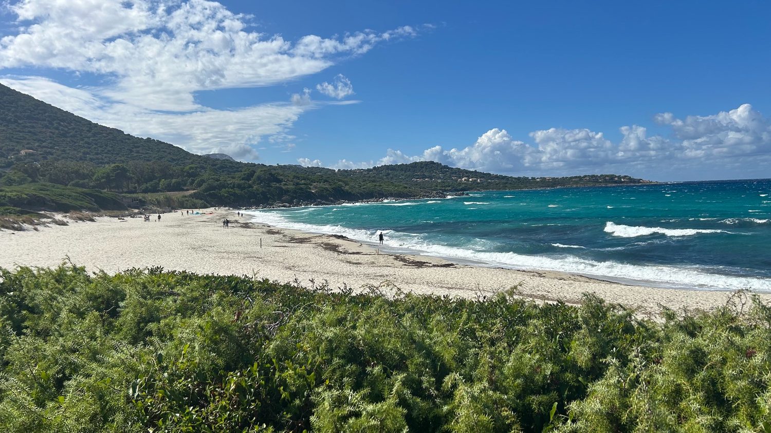 Sandstrand mit türkisem Meer und grünen Hügeln